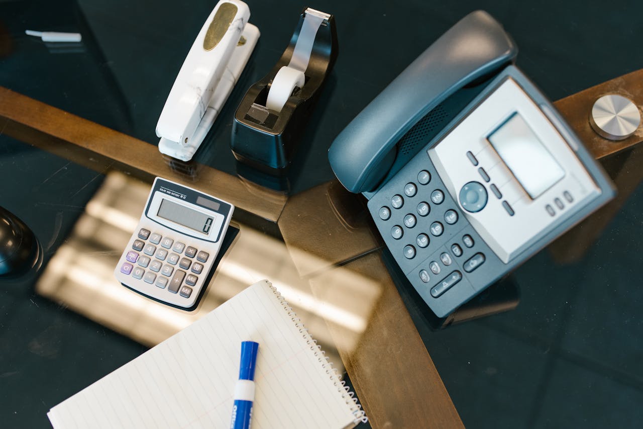 about-02 A neatly arranged office desk with a calculator, phone, stapler, tape, and notepad.