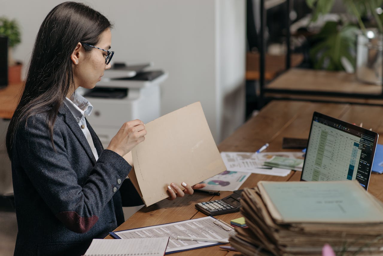 A professional woman reviewing documents at her office desk with a laptop and files.